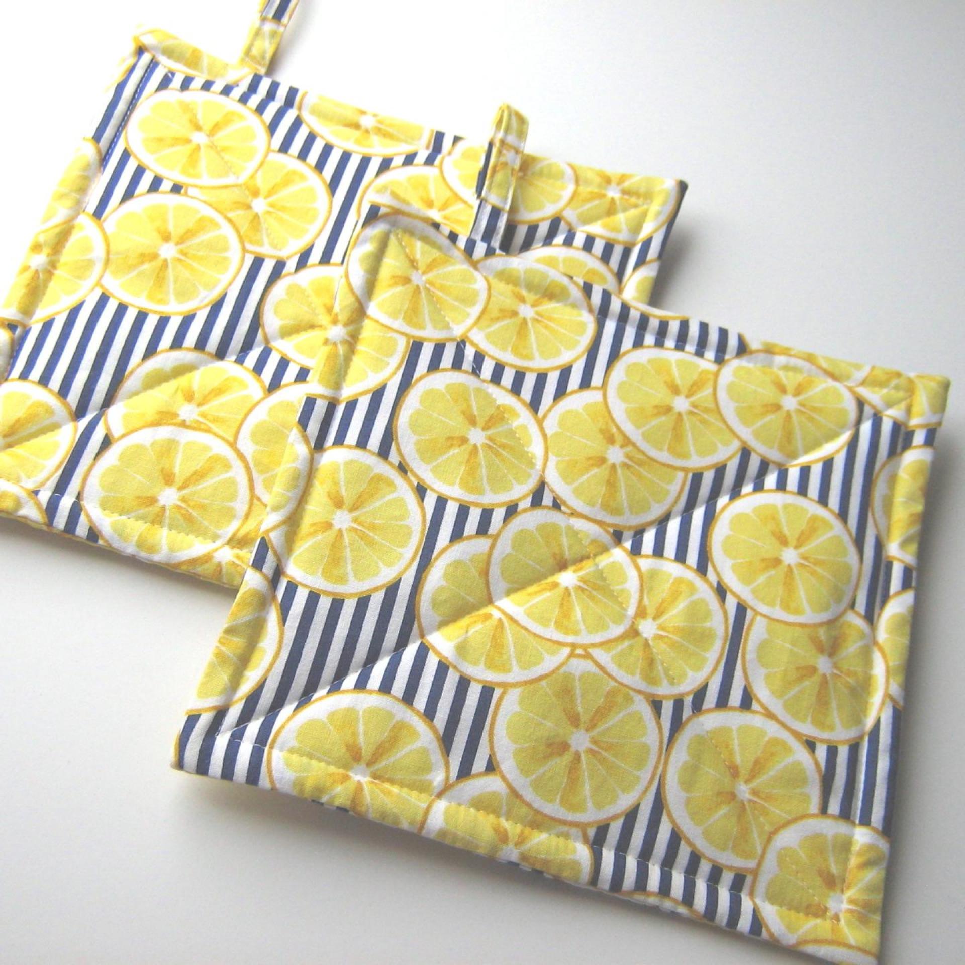 2 overlapping squares of padded fabric with thin vertical blue and white stripes partially covered by randomly placed images of yellow lemon slices. Hanging tabs on the upper edge.